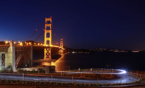 Light trails on illuminated city against clear sky at night