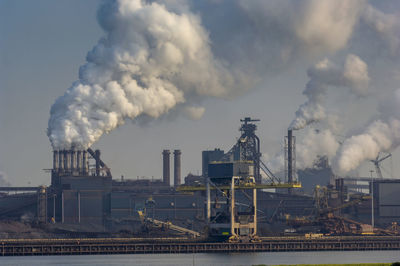 Smoke emitting from factory against cloudy sky