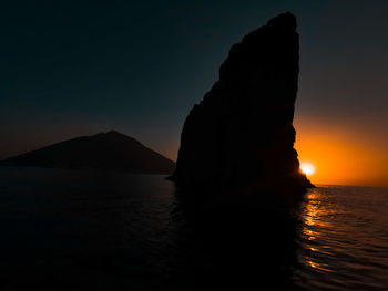 Silhouette rock in sea against sky during sunset