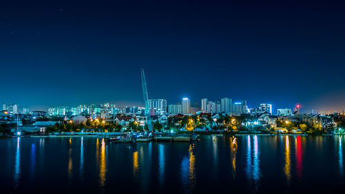Illuminated city by river against clear sky at night