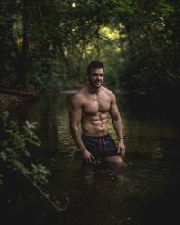 Full length of shirtless man in lake at forest