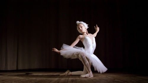 In rays of spotlight, on the stage of the old theater hall. young ballerina in suit of white swan