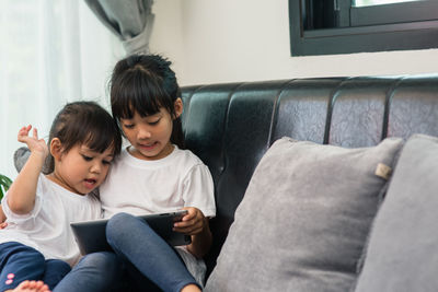 Siblings learning over digital tablet while sitting on sofa