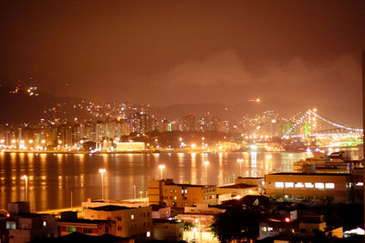 Illuminated cityscape by sea against sky at night