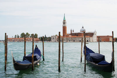 Gondolas moored in canal against sky