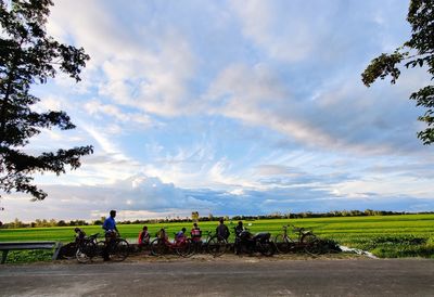People riding bicycle on field against sky
