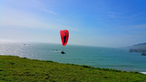 Scenic view of paraglidier with red sail over sea against sky