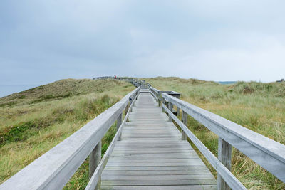 Boardwalk amidst grassy field against sky