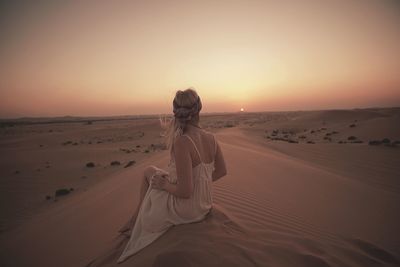 Woman sitting on sand dune against sky