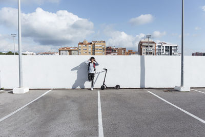 Young man with e-scooter and headphones on parking deck