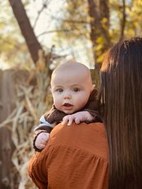 Cute baby boy looking over moms shoulder on an autumn day