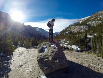 Side view of hiker standing on rock against mountains on sunny day