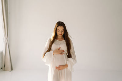 Cute young pregnant girl sitting on the white studio in warm light