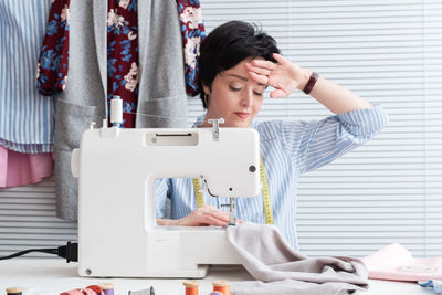 Worried craftswoman sewing textile on machine at workshop