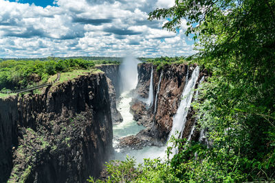 Scenic view of waterfall against cloudy sky