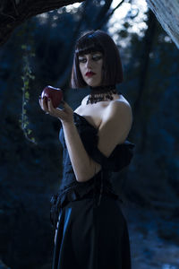 Smiling woman holding apple standing against trees in forest