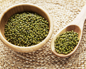 Raw mung beans in the wooden bowl on a straw mat background