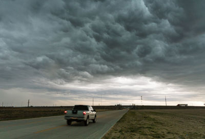 Road passing through field against cloudy sky