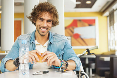 Portrait of smiling man having burger at table in cafe
