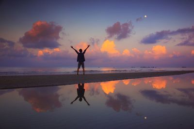 Silhouette man standing in sea against sky during sunset