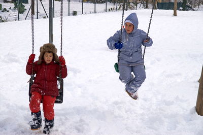 Full length of friends sitting on swing during winter