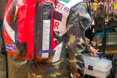 Midsection of army solider holding first aid kit outdoors