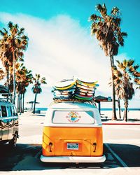 Yellow car on street by palm trees against sky