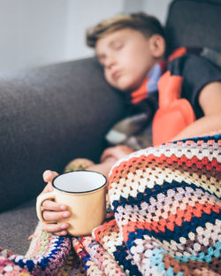 Sick boy sleeping with woolen blanket, with hot mug in hand. sad teen with flu rests alone at home. 