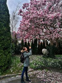 Full length of woman standing by pink flowers in park