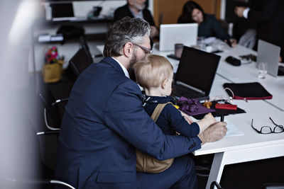 Businessman with son working at conference table while colleagues in background