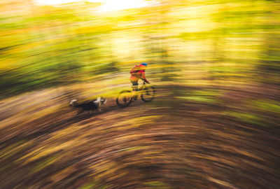 Blurred female mountain-biking downhill with dog running behind