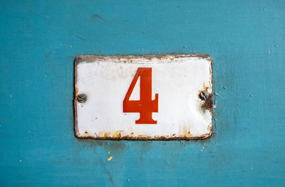 Close-up of rusty sign with number 4 on blue wall