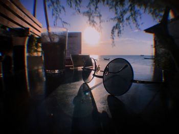 Chairs and table by sea against sky during sunset