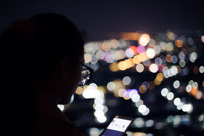 Woman using mobile phone with illuminated lights at night