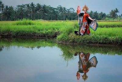 Reflection of female model standing in traditional clothing on lake