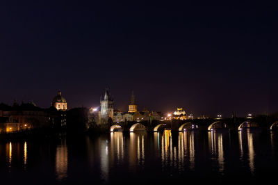 Illuminated city by river against sky at night