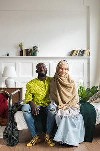 Portrait of smiling couple sitting on bed at home