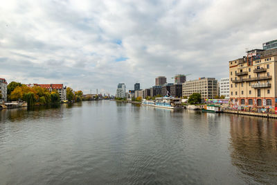 Buildings by river against cloudy sky