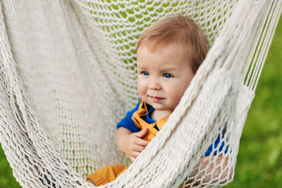 A little boy sits in a hammock on a summer day in the garden