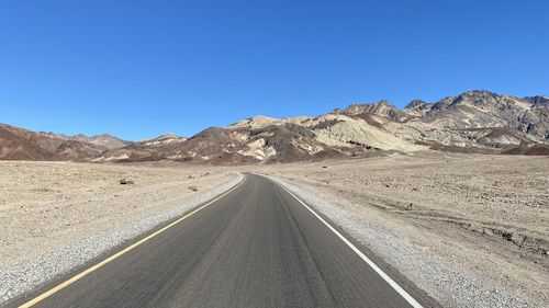 Road leading towards mountains against clear blue sky