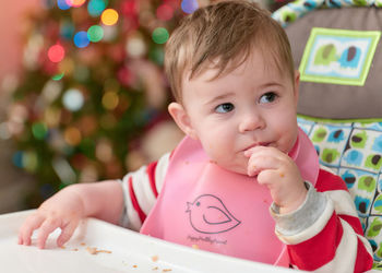Little boy toddler eating in his high chair in front of the christmas tree
