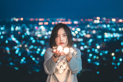 Close-up of young woman holding illuminated lighting equipment at night