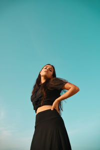 Low angle view of woman in black dress standing against clear sky