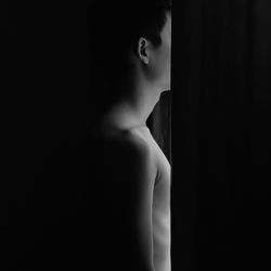 Side view of shirtless young woman against black background