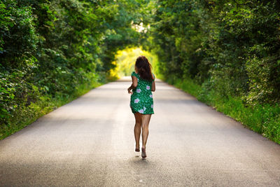 Rear view of woman running on road amidst trees