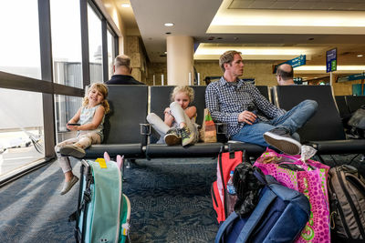 Two girls and father sitting in airport terminal waiting to board