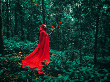 Woman with red cape standing by plants in forest