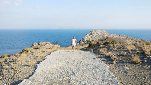 Rear view of woman walking towards sea against sky