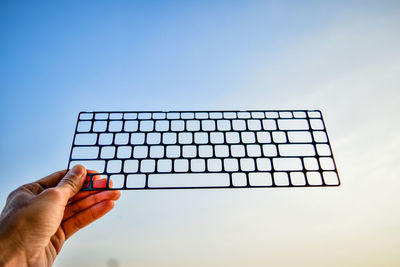 Cropped hand holding keyboard frame against sky