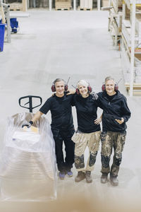 High angle portrait of smiling male and female workers standing with pallet jack in industry